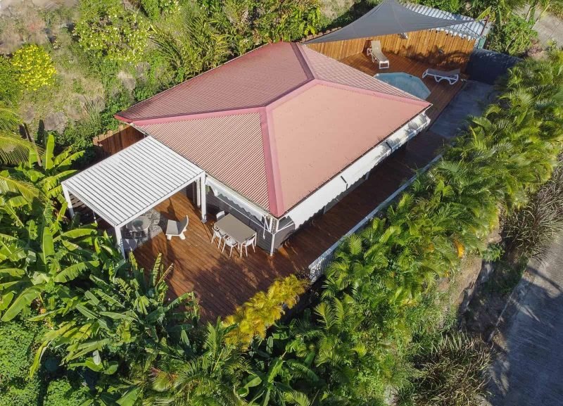 Villa O Perchée – Vue aréienne Balcon en bois avec mobilier extérieur, décoration élégante et vue sur la végétation tropicale, parfait pour profiter d'un séjour relaxant en Guadeloupe.